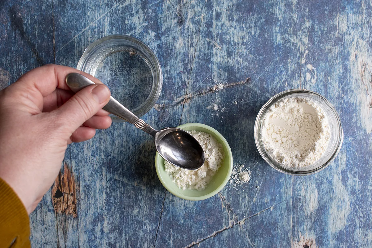 woman's hand spooning water over flour in a small mixing cup.