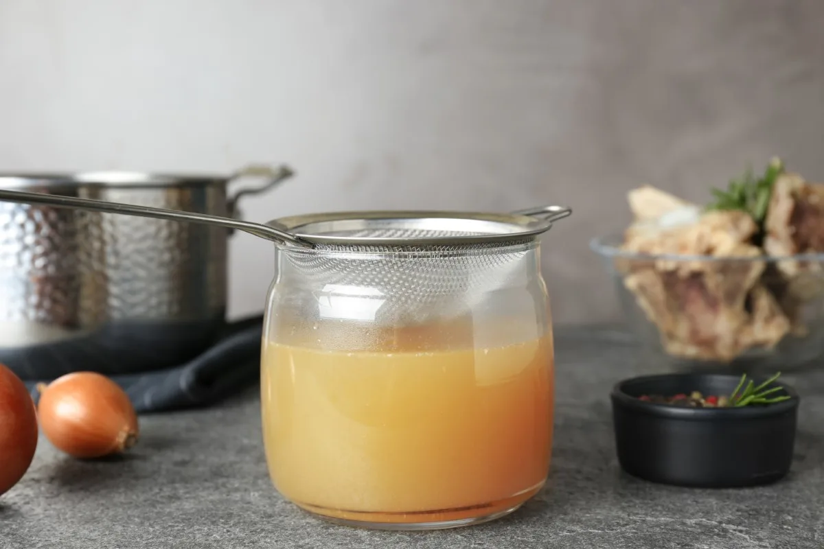 Strainer over jar filled with bone broth.