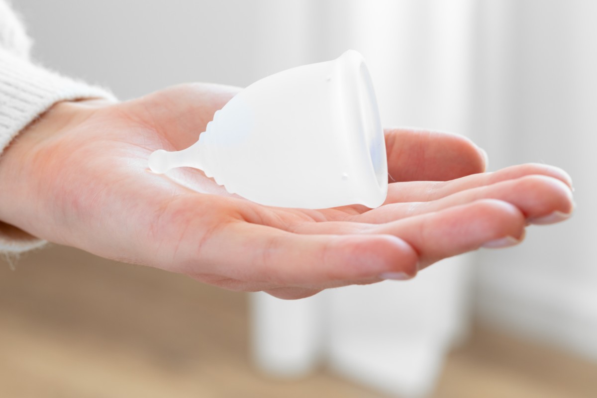 A woman's hand holding a clear silicone menstrual cup. 
