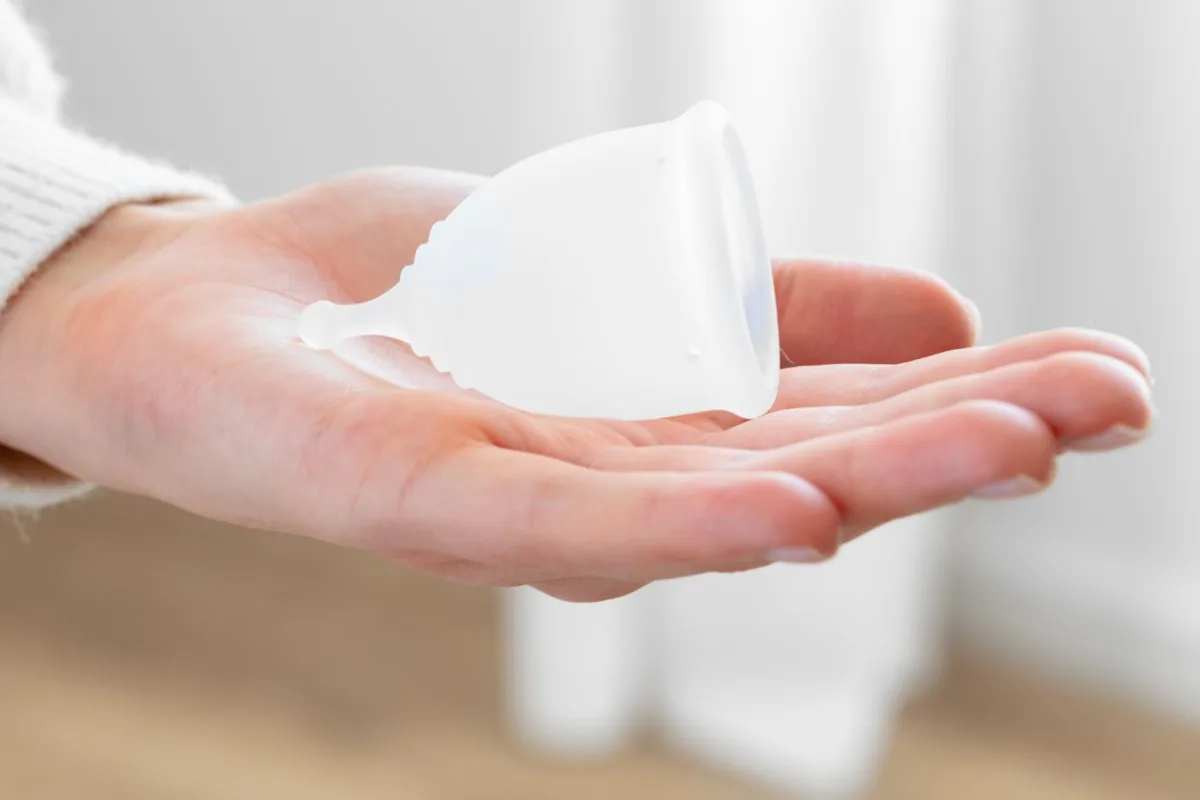 A woman's hand holding a clear silicone menstrual cup. 
