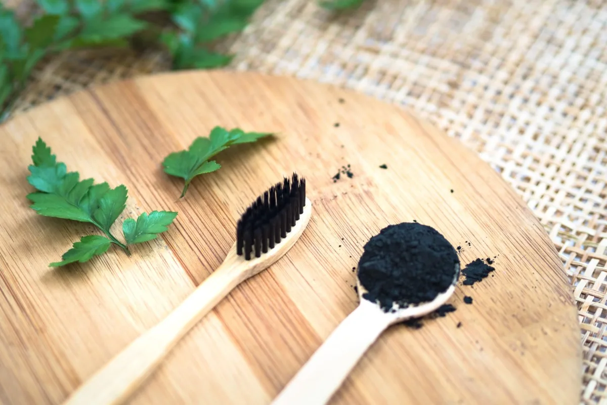 A bamboo toothbrush and a bamboo spoon with charcoal tooth powder.