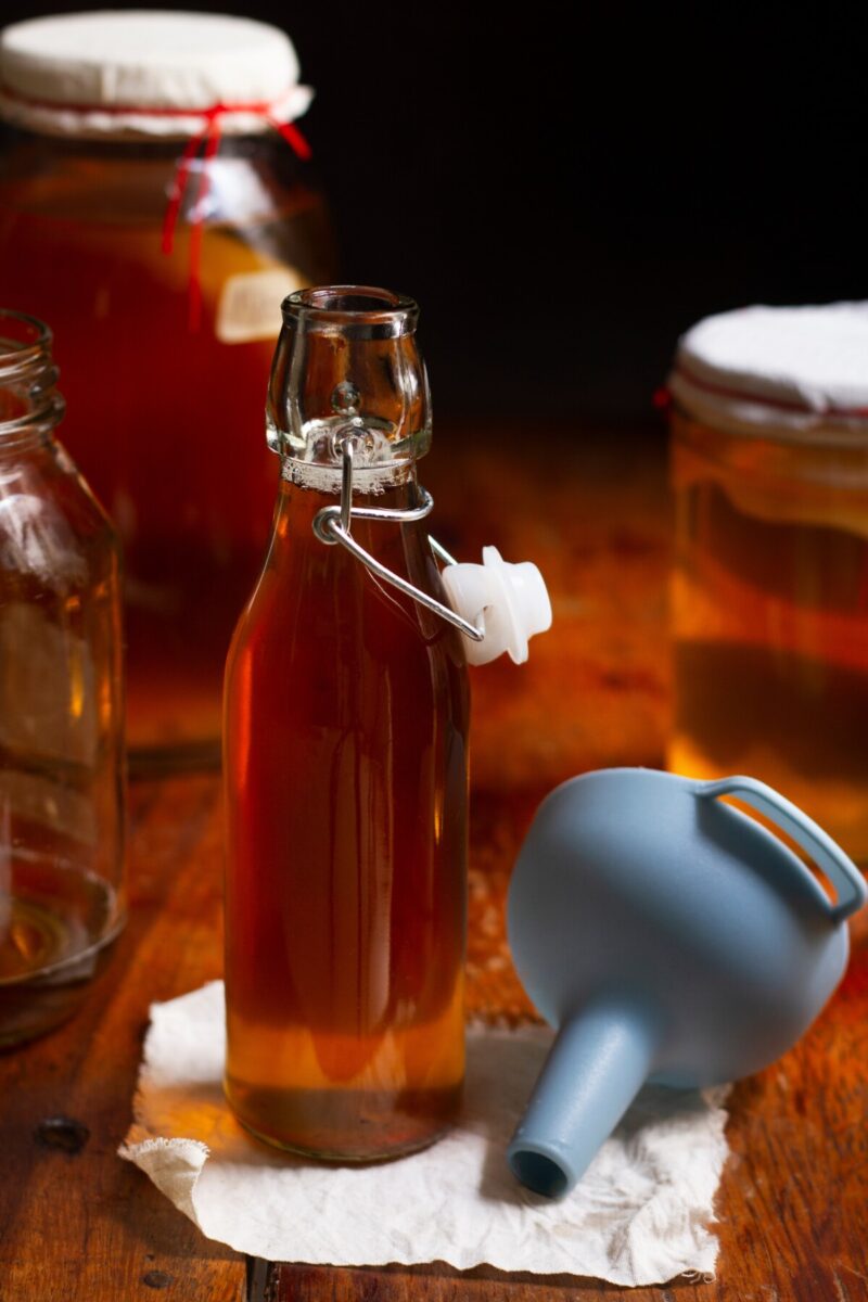 Swing-top bottle filled with kombucha next to a blue funnel