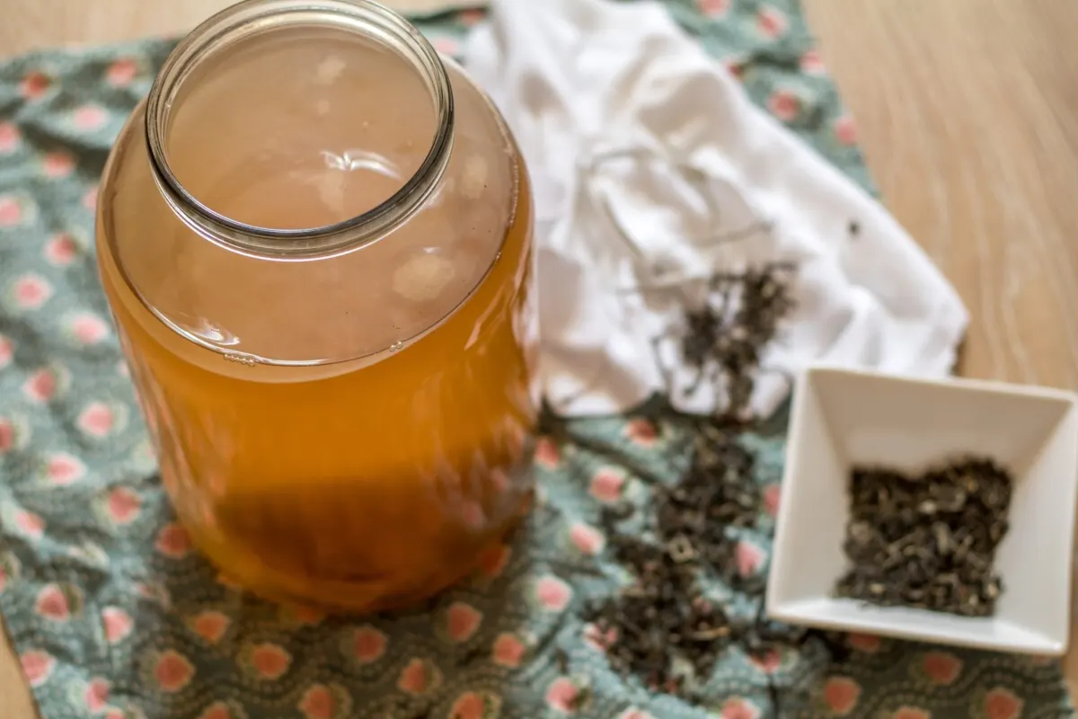 Jar of starter liquid and pellicle next to a dish of green tea leaves. 