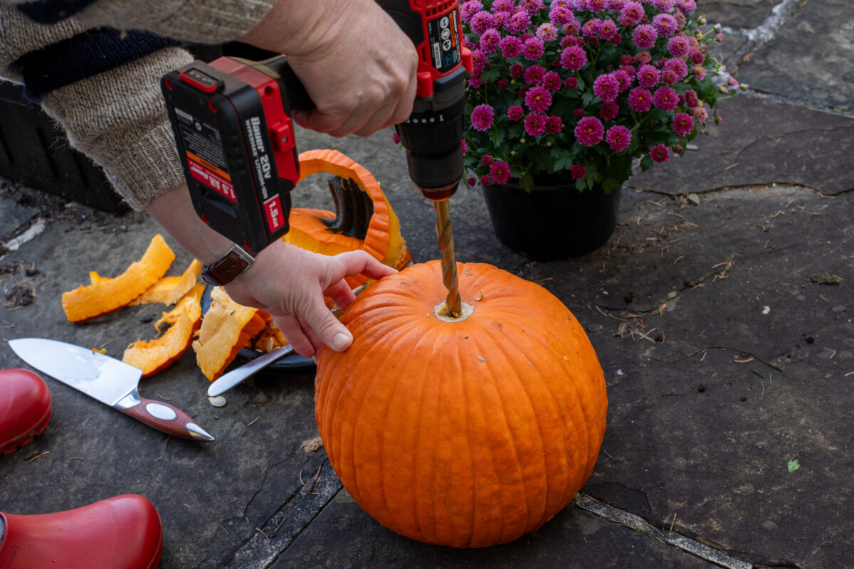 Woman using a drill to put a drainage hole in the bottom of a pumpkin.