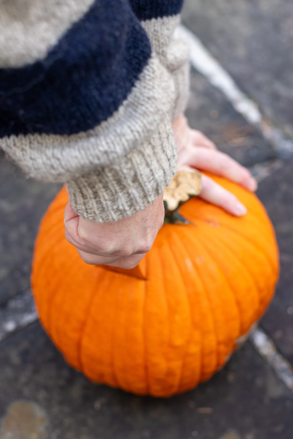 Woman using a large knife to cut a hole in the top of a pumpkin.