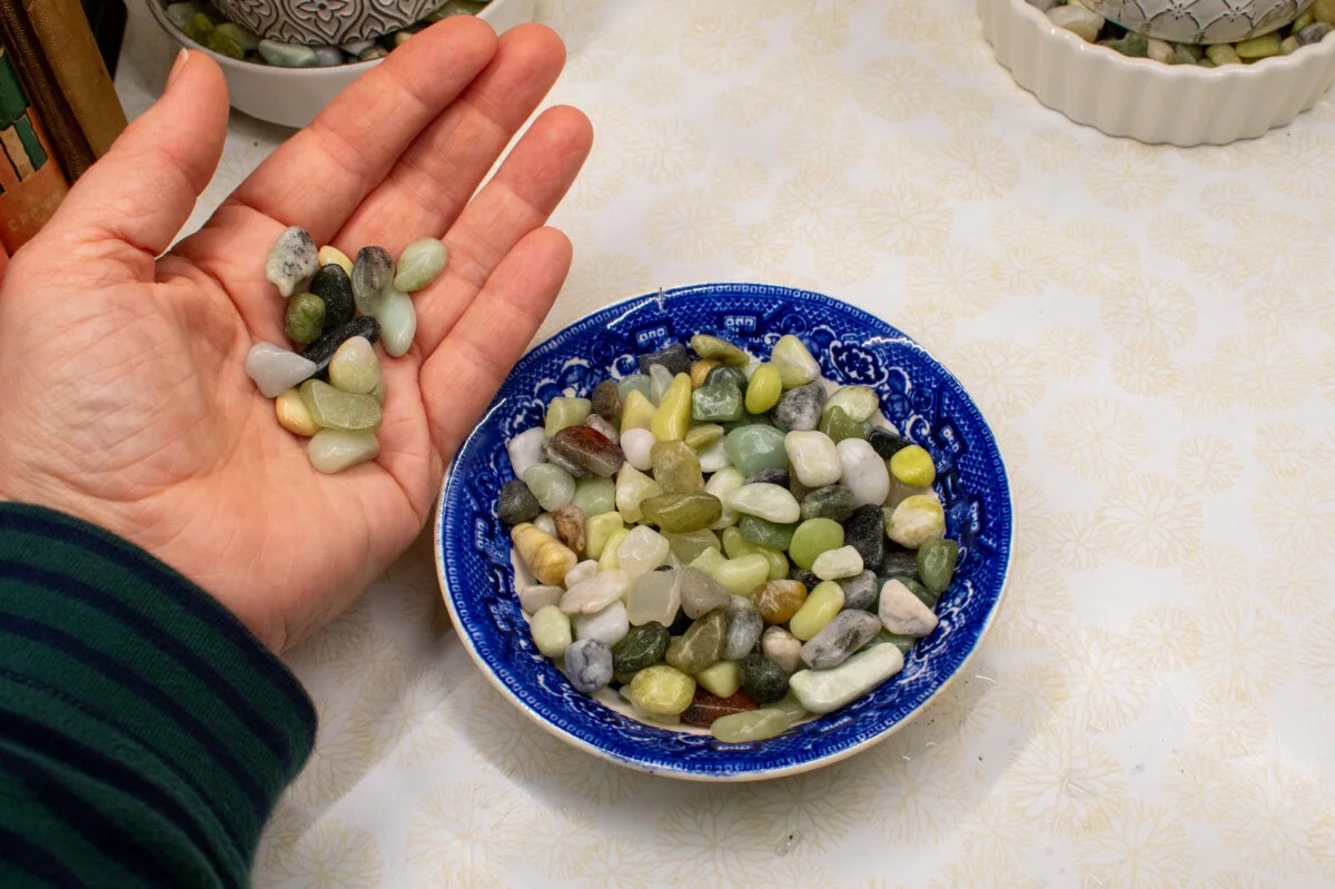 woman's hand holding pebbles, a dish with pebbles in it